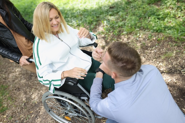 El hombre se comunica con la mujer discapacitada sonriente en una silla en el apoyo del parque para personas con