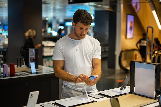 Hombre concentrado eligiendo smartphone en tienda de electrónica