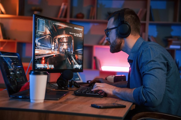 Hombre concentrado está jugando el juego de disparos en su computadora iluminación de neón
