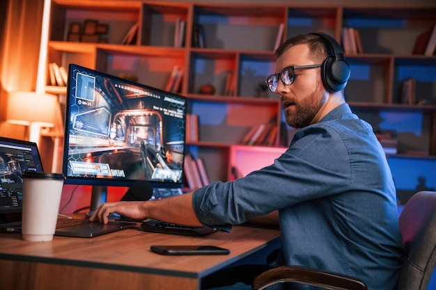 Hombre concentrado está jugando el juego de disparos en su computadora iluminación de neón