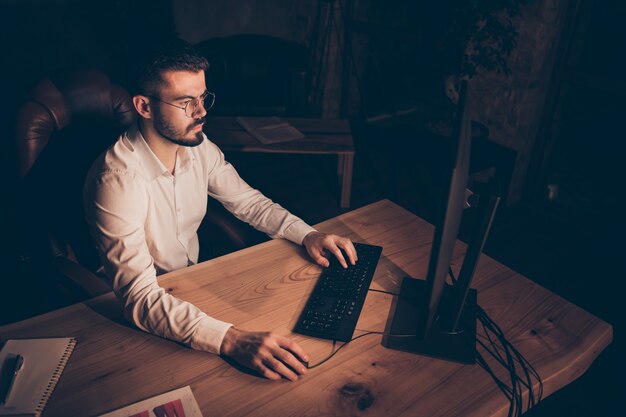 Hombre concentrado en la oficina de noche sentarse mesa trabajo pc