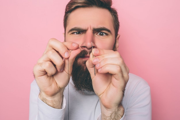 Hombre concentrado poniendo el hilo en el ojo de una aguja