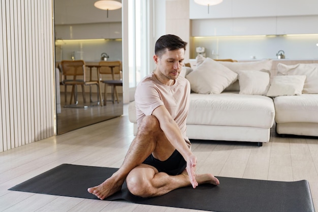 Un hombre concentrado practica yoga sentado estirándose en una alfombra armonizando la mente y el cuerpo en un hogar tranquilo