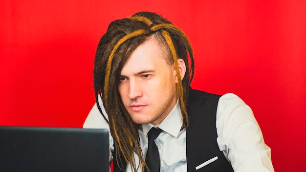 Hombre conceptual joven en traje de negocios que trabaja en el fondo rojo de la computadora portátil El profesional independiente de negocios trabaja de forma remota en el lugar de trabajo moderno