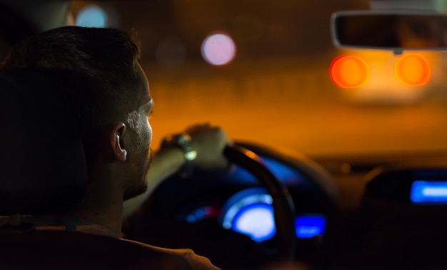 El hombre conduce un coche en la ciudad de la tarde.