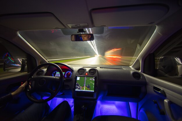 El hombre conduce con una navegación por la carretera. Vista interior. Por la noche, por la noche