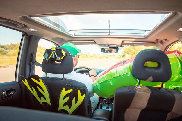 Hombre conduciendo un coche lleno de cosas de vacaciones en el mar