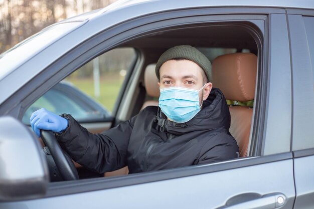 Hombre conduciendo un coche con una máscara médica y guantes durante una epidemia