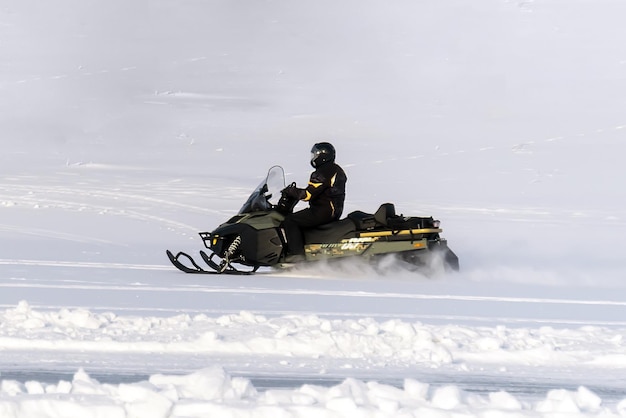 Hombre conduciendo motos de nieve deportiva en la Laponia finlandesa en un día soleado. moto de nieve en un campo en la nieve. Competiciones en motos de nieve. Entretenimiento extremo de invierno