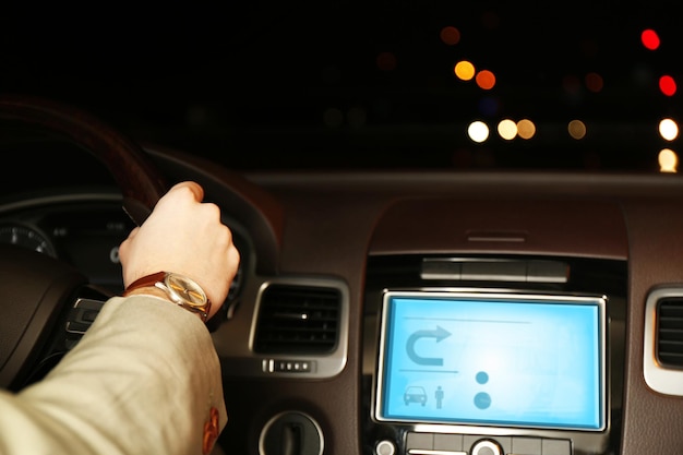 Hombre conduciendo su coche moderno por la noche en el primer plano de la ciudad