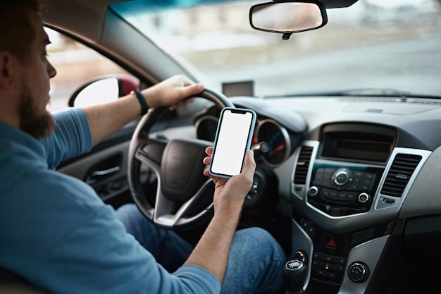 Hombre conductor que usa una maqueta en blanco de la pantalla del teléfono móvil en la carretera mientras conduce un automóvil