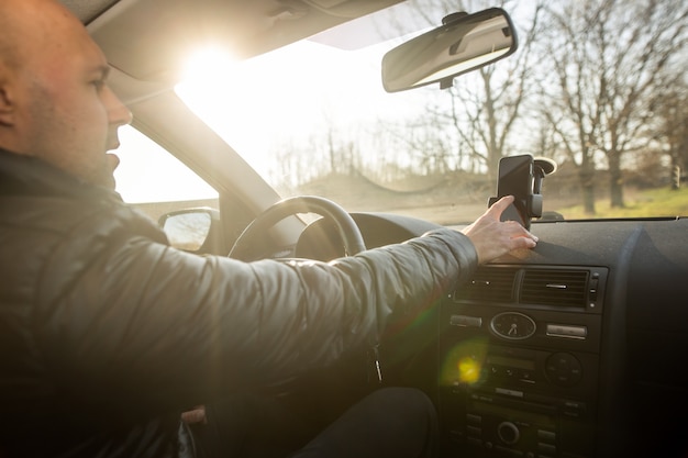 El hombre configura el GPS en el móvil antes de conducir, asisstant durante la conducción del automóvil, concepto de transporte