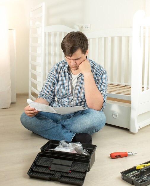 Hombre confundido acerca de cómo ensamblar muebles leyendo el manual