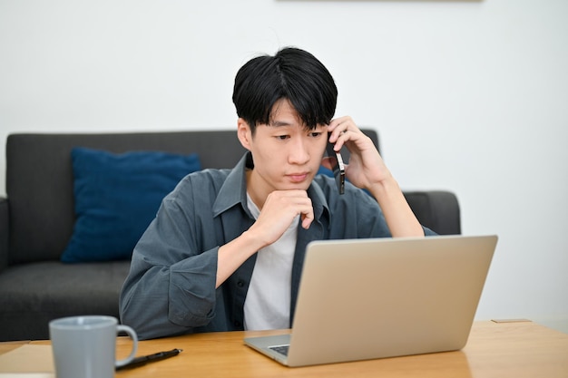 Hombre confundido mirando la pantalla de la computadora portátil mientras hace una pregunta por teléfono con un compañero de trabajo