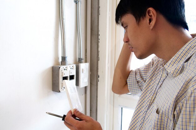 Un hombre confuso para arreglar el interruptor eléctrico en la pared.