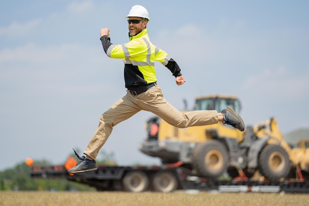 El hombre de la construcción emocionado salta con el constructor del casco en el casco, trabaja al aire libre en casco rápido runni