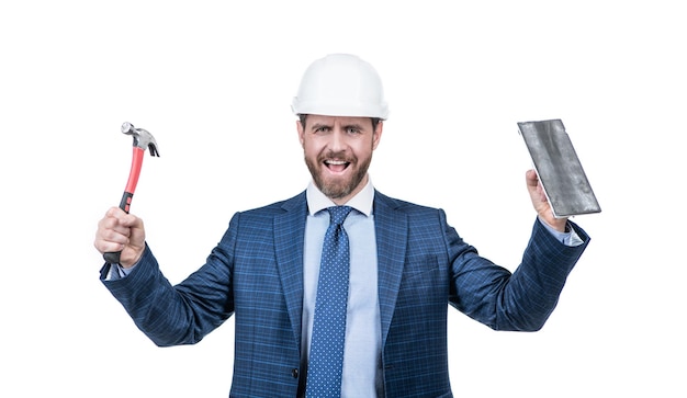 El hombre de la construcción feliz usa casco de seguridad con traje formal con martillo y paleta aislado en un edificio blanco