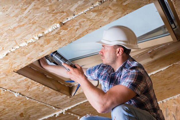 Hombre constructor de trabajador de la construcción aplicando masilla fresca a la luz del cielo en el techo de la casa sin terminar