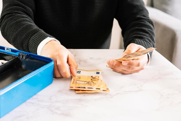 Hombre contando billetes junto a una caja de seguridad metálica en una mesa