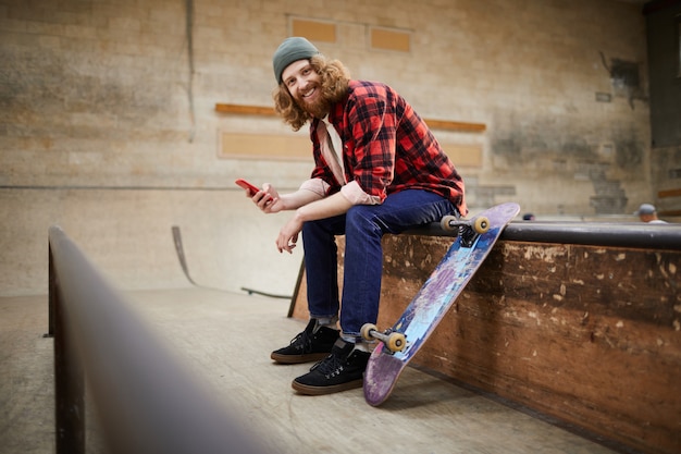 Hombre contemporáneo posando con smartphone en el parque de patinaje