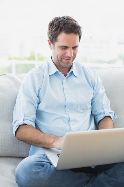 Hombre contento que usa la computadora portátil que se sienta en el sofá