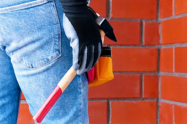 Un hombre en el contexto de una pared de ladrillo rojo con una bolsa llena de herramientas.