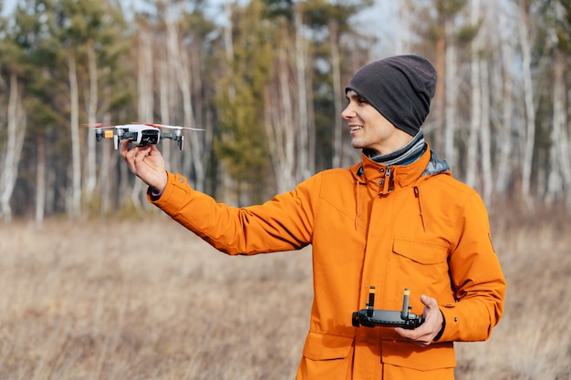 Un hombre controla un avión no tripulado quadcopter al aire libre en otoño. El chico extiende su mano hacia el dron.