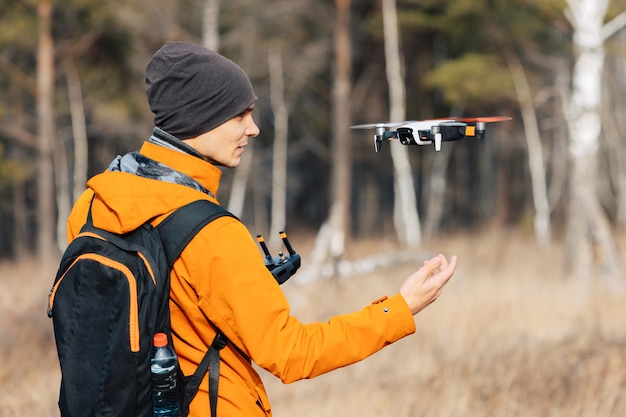 Un hombre controla un avión no tripulado quadcopter al aire libre en otoño. El chico extiende su mano hacia el dron.