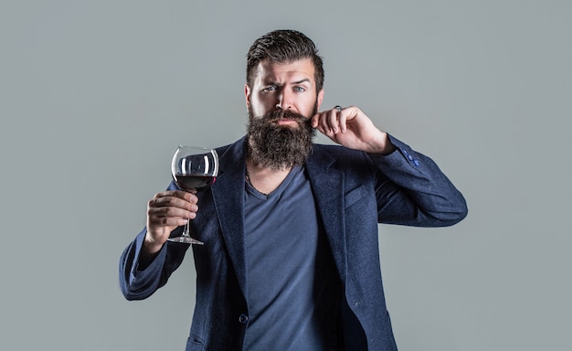Hombre con una copa de vino tinto en sus manos. Hombre de barba, barbudo, sumiller degustación de vino tinto. Sumiller, degustador con copa de vino, bodega, enólogo masculino.