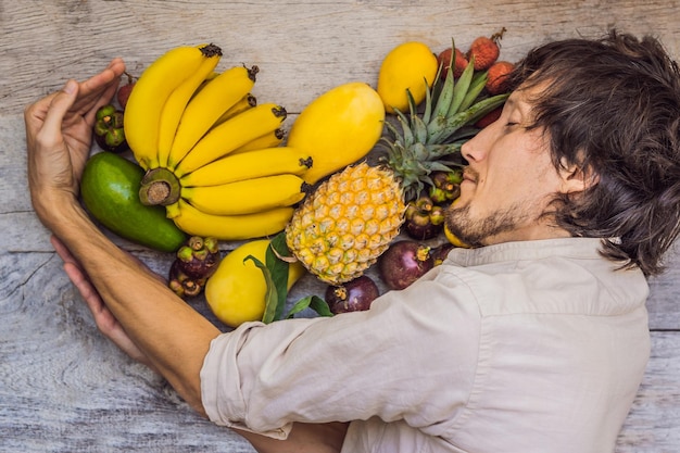 Hombre y corazón hecho de muchas frutas sobre fondo de madera