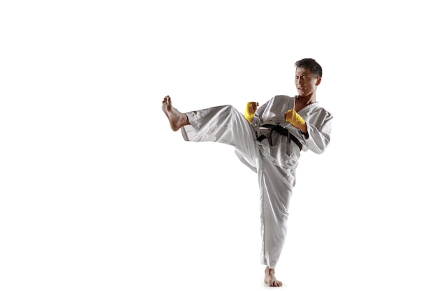 Hombre coreano confiado en kimono practicando combate cuerpo a cuerpo, artes marciales. Luchador masculino joven con entrenamiento de cinturón negro aislado sobre fondo blanco de estudio. Concepto de estilo de vida saludable, deporte.