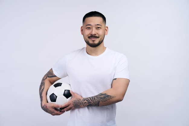 Hombre coreano feliz posando con balón de fútbol y mirando a la cámara