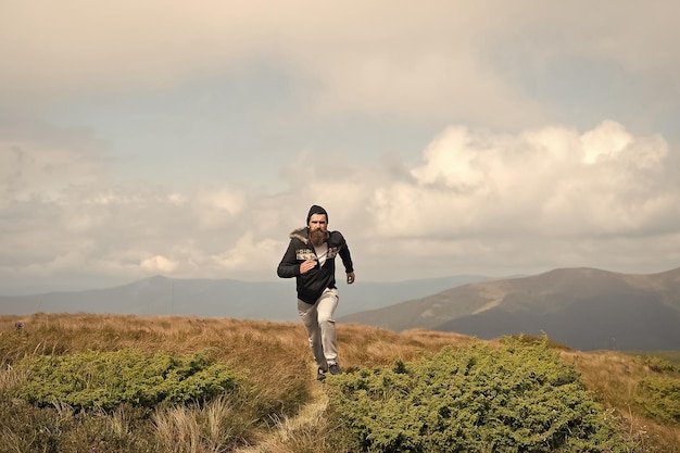 El hombre corre en el prado verde en la montaña en el cielo nublado