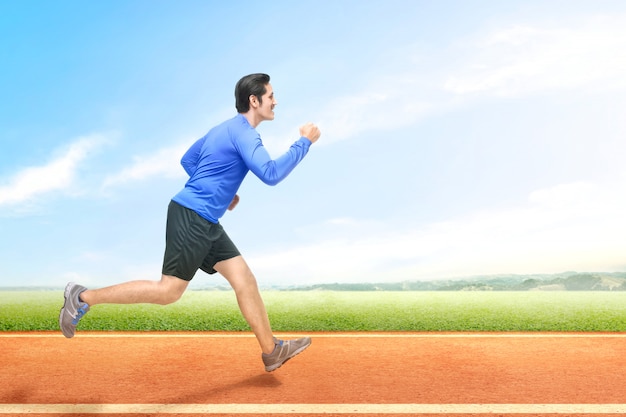 Hombre corredor asiático corriendo en la pista de atletismo