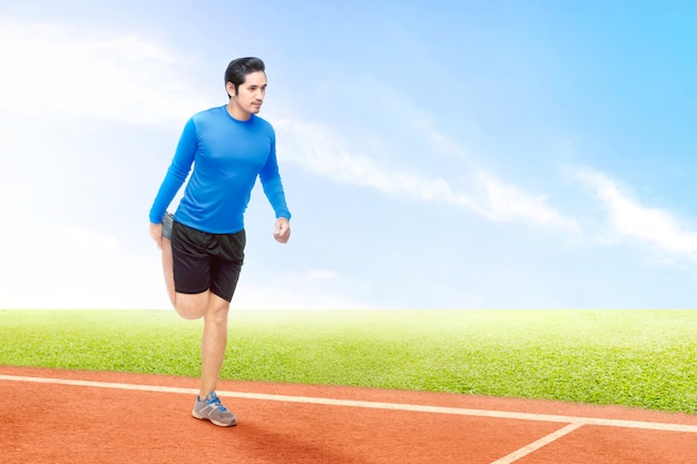 Hombre corredor asiático estirando las piernas antes de comenzar la carrera en la pista de atletismo