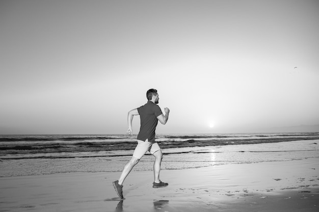 Hombre corredor jogger corriendo en forma corredor de fitness masculino durante el entrenamiento al aire libre con fondo de puesta de sol en el mar