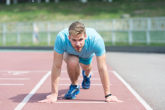 Hombre corredor en posición de inicio en el estadio Corredor en pose de inicio en la superficie de carrera Hombre correr al aire libre en la pista de atletismo Concepto de deporte y atletismo Deportista en cara concentrada listo para correr