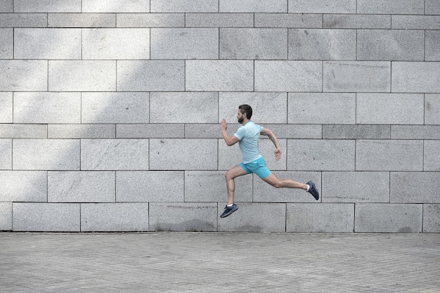 Hombre corriendo al aire libre. Corredor masculino sano. darse prisa. Retrato de cuerpo entero de chico fitness corriendo. Logro del éxito y la excelencia. Atleta corriendo contra la pared de hormigón. El hombre deportivo comienza a correr.