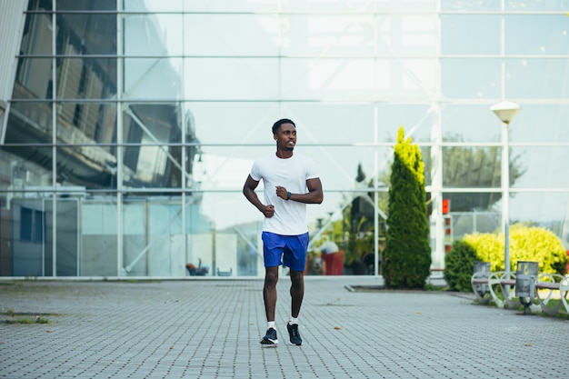 Hombre corriendo por la mañana, joven atleta afroamericano corriendo cerca del estadio