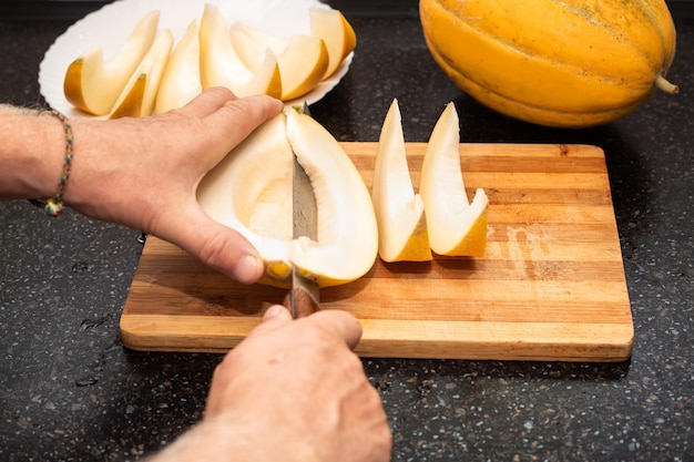 Un hombre corta un melón jugoso maduro en rodajas en una tabla de madera Deliciosa comida saludable