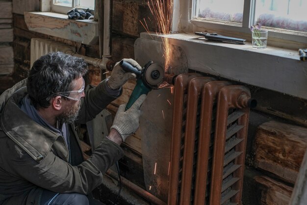 Un hombre corta radiadores viejos en su casa de madera con una amoladora angular y un disco de corte