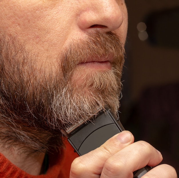 Un hombre corta su recortador de barba gris de cerca