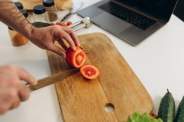 Un hombre corta un tomate rojo en un tablero.