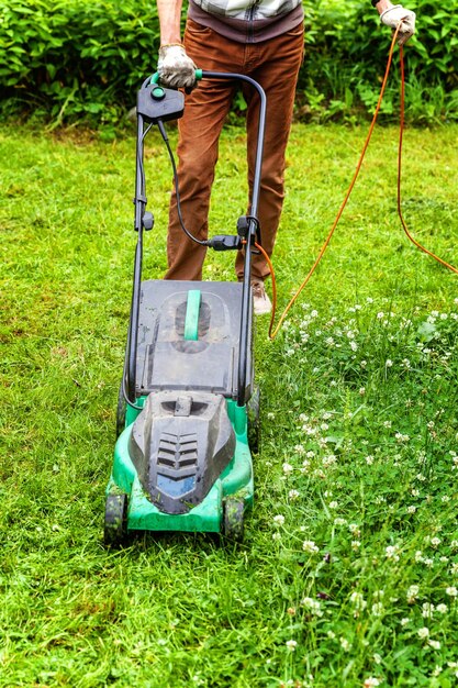 Hombre cortando hierba verde con cortadora de césped en el patio trasero Fondo de estilo de vida rural de jardinería Hermosa vista sobre césped de hierba verde fresca en el paisaje del jardín de la luz del sol en primavera o verano