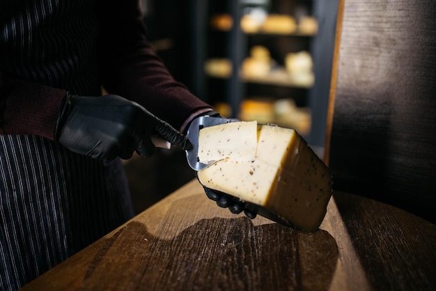 Hombre cortando un pequeño trozo de queso para probarlo Un joven trabajador usa un cuchillo especial para queso