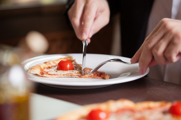 Hombre cortando una rebanada de pizza con cuchillo y tenedor