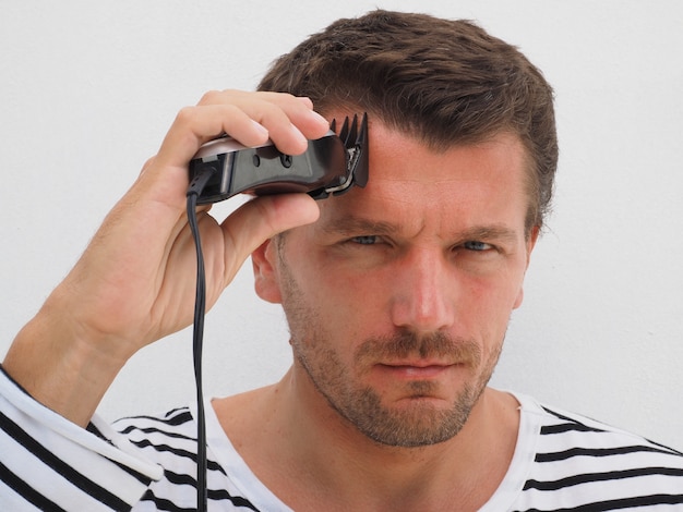 Hombre cortando su propio cabello con una podadora. Estilo de vida.