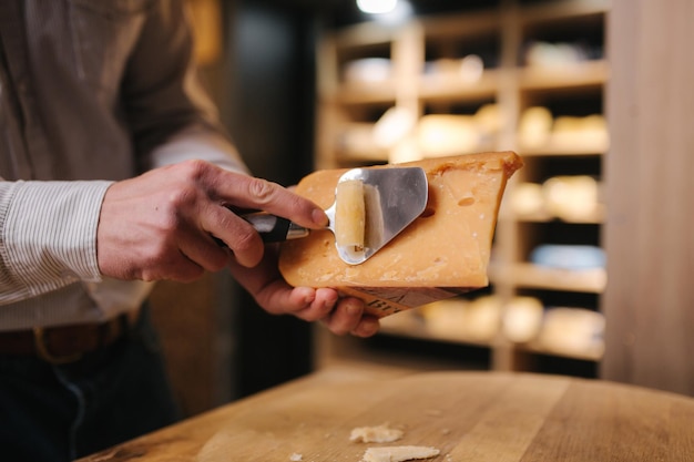 Hombre cortando un trozo de queso para saborear El trabajador joven usa un cuchillo especial para queso