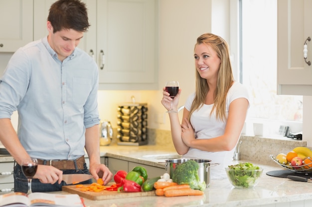 Hombre cortar verduras con mujer bebiendo vino