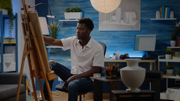 Hombre creativo afroamericano que usa un jarrón para inspirarse mientras está sentado en el espacio de la obra de arte. Adulto joven negro con visión artística trabajando en bellas obras maestras de lienzo y bellas artes